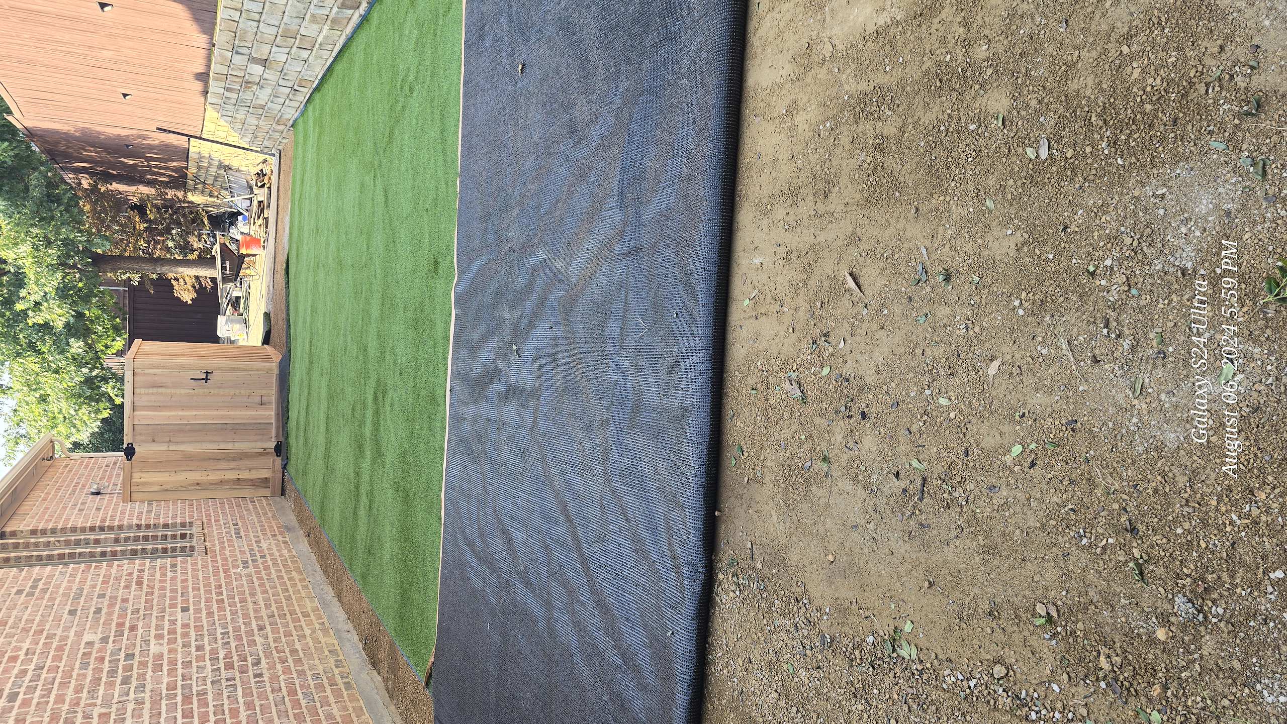 Artificial turf being installed in a backyard next to a brick house and wooden shed.