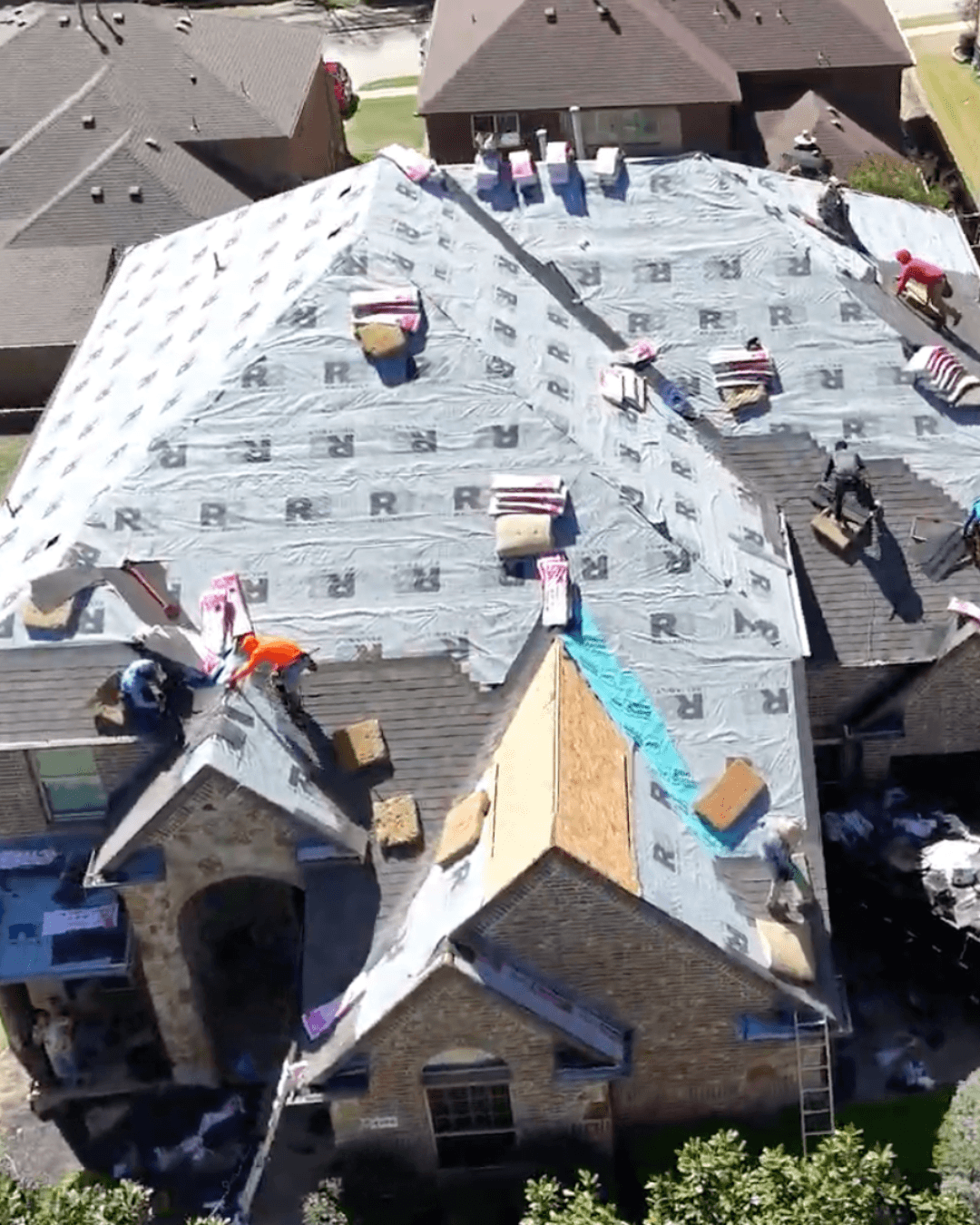 Roofing contractors installing new shingles and grey underlayment on a large suburban home's roof.