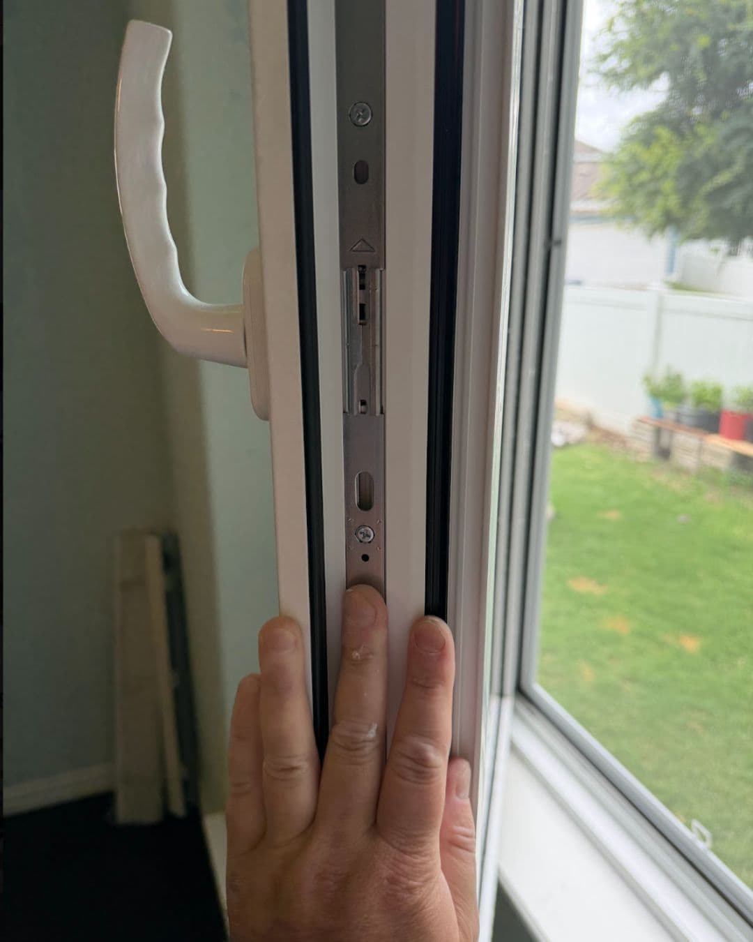 Hand touching the internal metal locking mechanism of an open white window frame.